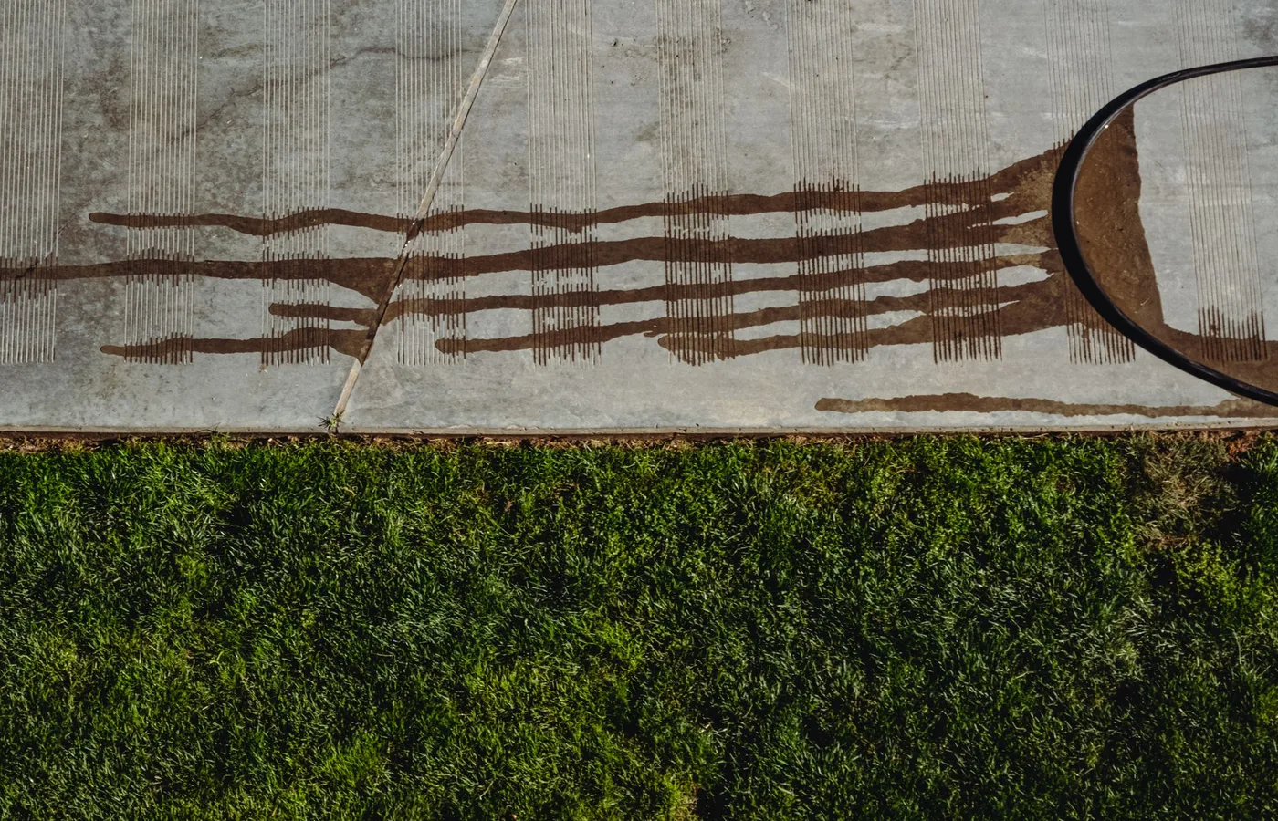 Dirty water running in streaks across a pale concrete slab beside a green lawn
