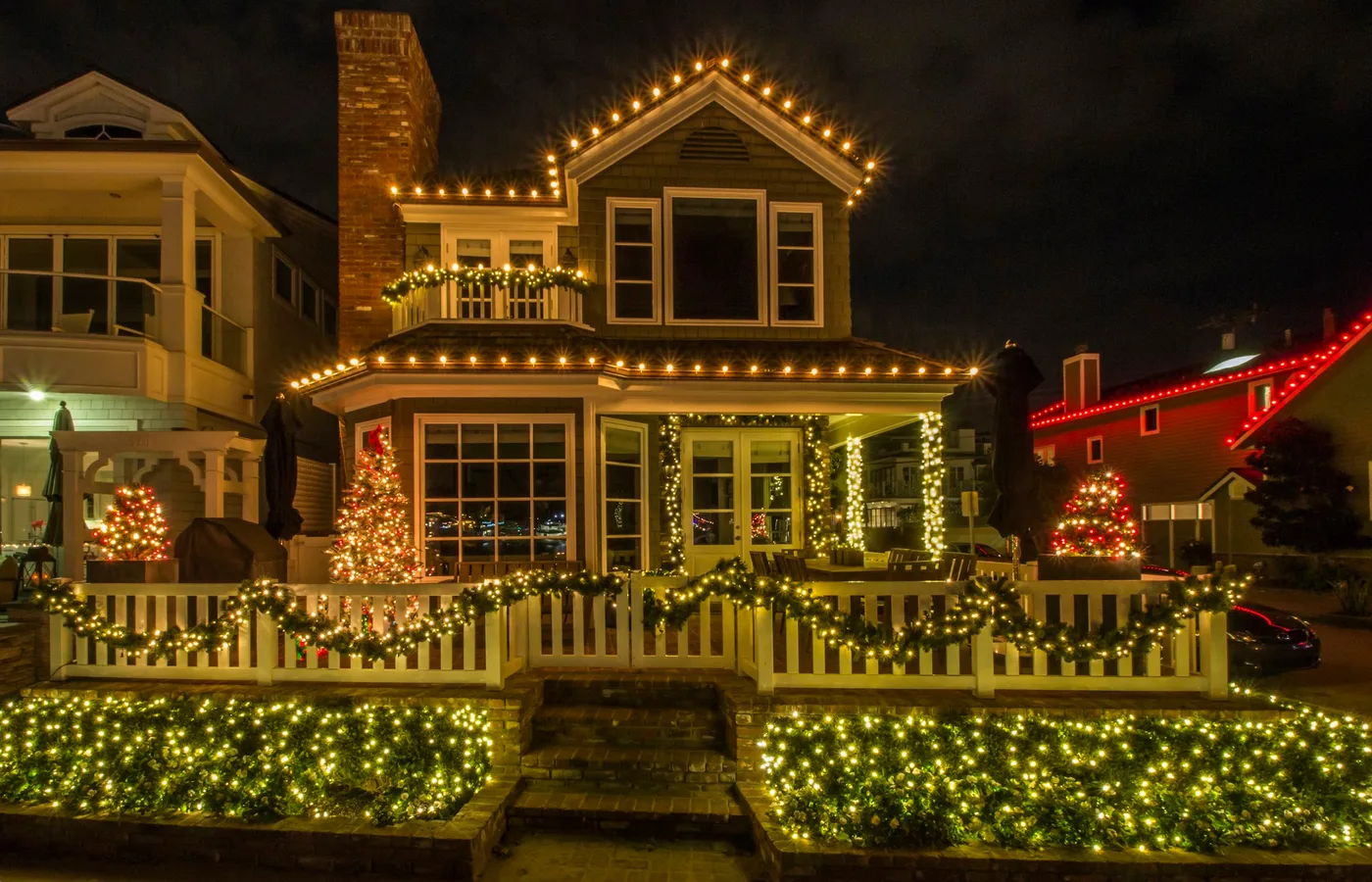 Two-story home outlined in warm white Christmas lights along the roofline and porch at night