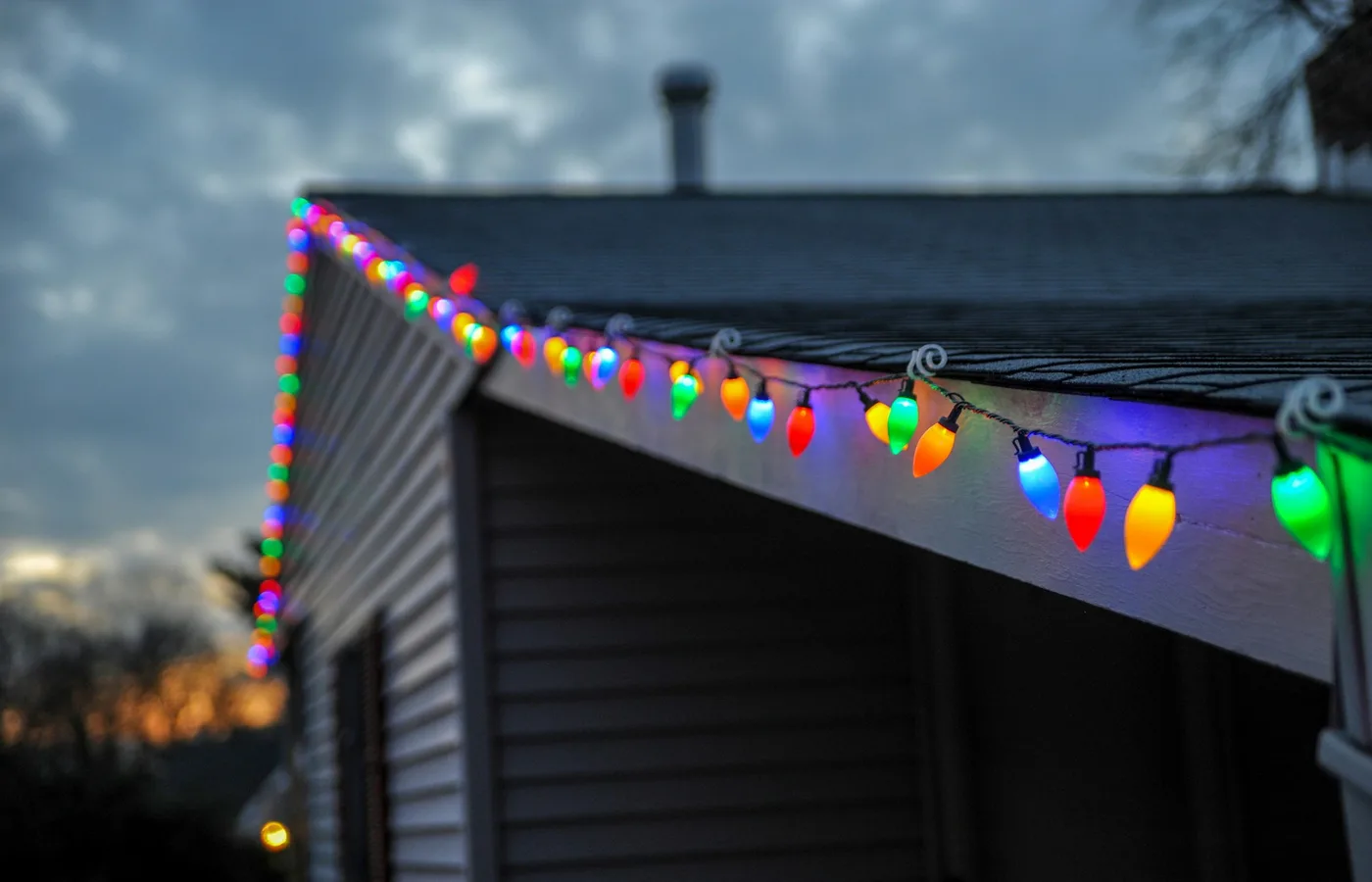 Coloured Christmas bulbs clipped along the edge of a roofline at dusk