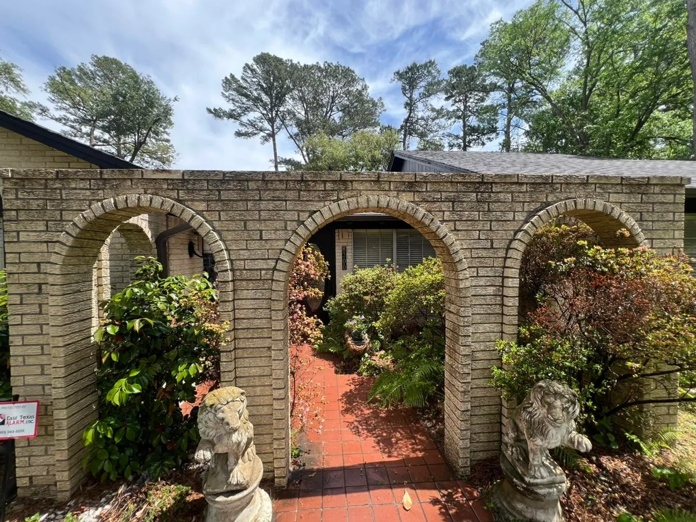 A brick breezeway of three arches with stone lions before washing, the brick greyed and the tile walk dull
