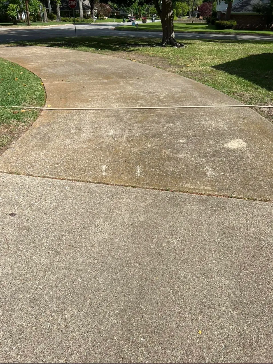 A concrete driveway before washing, grey and blotchy where it meets the street