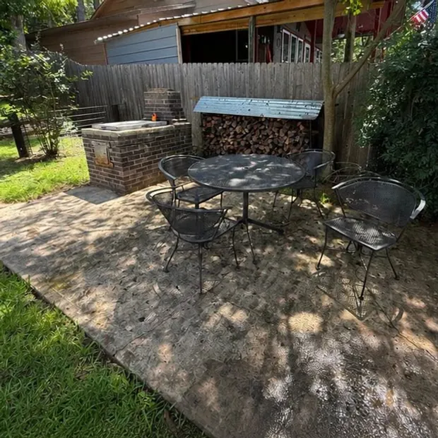 A backyard concrete patio before washing, dark and blotchy under a wood fence